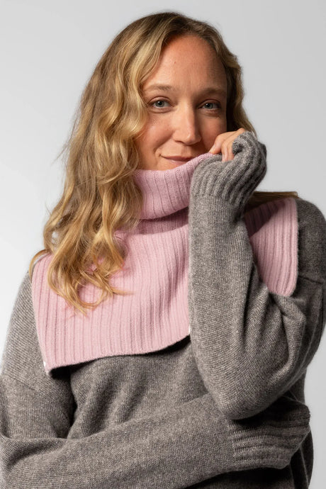 Female model wearing a soft, ribbed, dusty pink neckwarmer over a stone beige  jumper in pure cashmere.